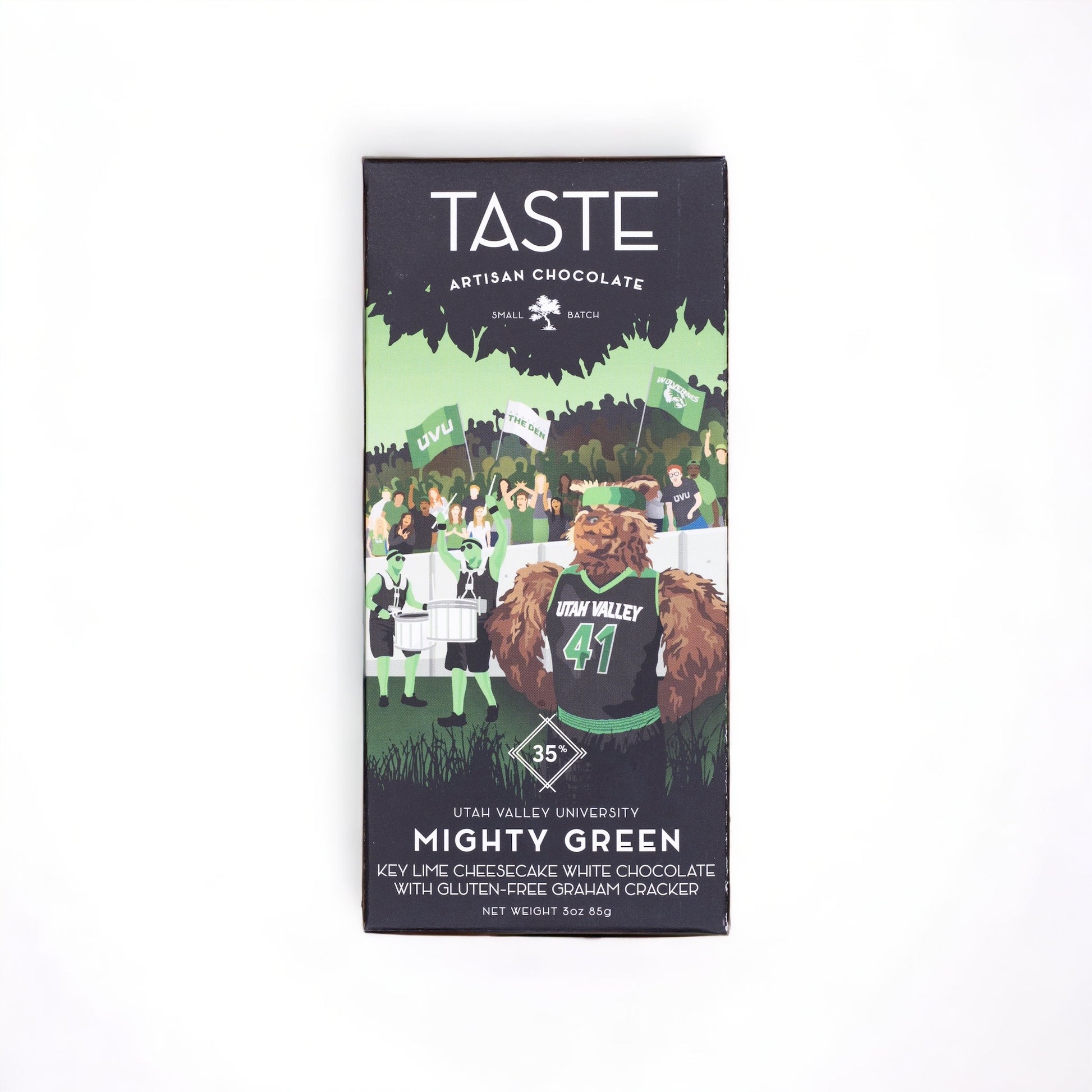 A packaged chocolate bar with the brand name TASTE on the top, and a graphic of a character resembling a bear wearing a student cap in front of a university setting backdrop. The product is named 'Mighty Green' and lists ingredients such as cacao, organic cane sugar, and honeycomb.